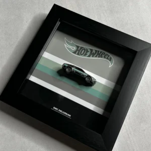 پوستر ۲۰×۲۰ سانتی‌متری با تصویر ماشین هات ویلز مدل DMC DeLorean مشکی، روی پس‌زمینه‌ای با نوارهای رنگی و لوگوی هات ویلز، در قابی مشکی.
